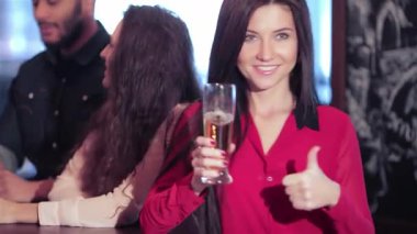 Neşeli bir arkadaş grubu, coşkulu bir barda bira bardağını kaldıran ve baş parmağını kaldıran genç bir kadınla kutlama yapıyor. En sevdikleri futbol topuna tezahürat ettikleri için ortam heyecan verici.