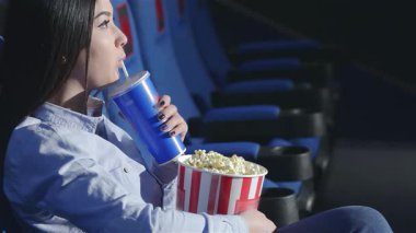 Asyalı bir kız profilde oturuyor, canlandırıcı bir soda yudumluyor ve canlı bir sinemada elinde büyük bir kova patlamış mısır tutuyor. Etrafı arkadaşlarla çevrili, atmosfer heyecan ve neşeyle dolu.