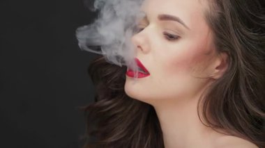 Bu çarpıcı ağır çekim sahnesinde, çekici esmer saçlı güzel beyaz bir kadın kameraya yoğun bir şekilde bakıyor, kusursuz cildi dramatik bir siyah arkaplan karşısında ışıldıyor. Görüntü