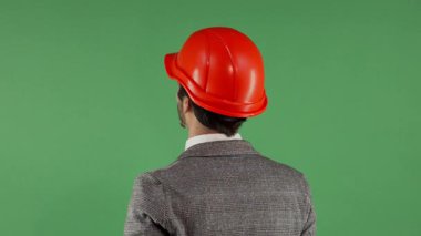 Şık bir takım elbiseli ve parlak turuncu kasketli bir erkek mühendisin dikiz görüntüsü, canlı yeşil renkli bir ekrana bakarken hayal kırıklığı içinde boynunu ovuyor. Bu resim özünü yakalar.
