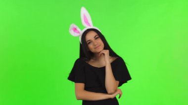 Göz kamaştırıcı genç bir kadın parlak siyah bir elbiseyle cazibesini sergiliyor, neşeli bir şekilde pofuduk tavşan kulakları takıyor parlak renkli bir arka plana karşı. Kendinden emin gülüşü ve hayat dolu duruşu flörtleşmeye yol açıyor.