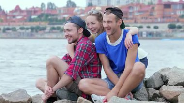 Üç genç arkadaş nehir kenarında neşeli bir anı paylaşıyor, kız neşe içinde arkadaşlarına sarılıyor ve hepsi gülümsüyor. Bu canlı sahne arkadaşlığın özünü yansıtıyor ve...