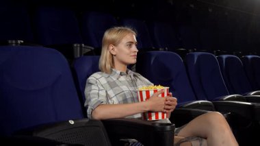 Neşeli bir gülümsemesi olan ışıl ışıl genç bir kadın, elinde canlı bir kova patlamış mısırla lüks bir sinema koltuğunda rahatça oturur. Sıcak daveti sizi tiyatronun sıcak ortamında unutulmaz bir film deneyimi için ona katılmaya davet ediyor.