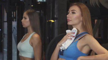 Uzun dalgalı saçlı neşeli genç bir sporcu, boynunu havluyla siler, yoğun bir spor seansından sonra memnuniyet saçar. Spor salonunun hareketli atmosferi, arka planda ağırlıklar, onun kararlılığını ve zindelik yolculuğunu arttırır.