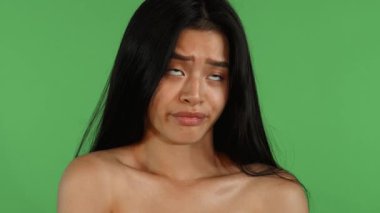 Uzun, dalgalı saçları olan çarpıcı bir Asyalı genç kadın canlı yeşil renkli bir arka plana karşı poz veriyor. Şüpheci ifadesi hayal kırıklığı yayıyor. Kusursuz cildi ve etkileyici özellikleri duygusal bir derinlik yakalıyor.