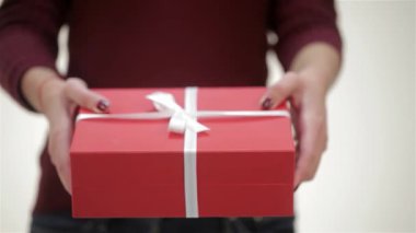 Yürek ısıtan yakın planda, parlak gülüşlü genç bir kadın canlı kırmızı bir hediye kutusu sunar. Zarif beyaz bir kurdeleyle süslenmiş. Bu şenlikli an, Noel gibi kış tatilleri için mükemmel olan kutlama ve aşkın özünü yakalar.