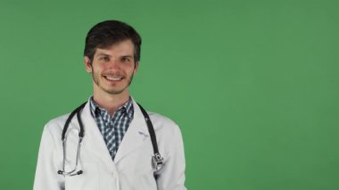 Genç, yakışıklı bir erkek doktor sıcak bir gülümseme ile ışınlar, elini canlı yeşil renkli bir arka plana doğru uzatır. Dostça tavrı ve profesyonel kıyafeti, steteskopla tamamlanmış, güveni davet ediyor ve özen göstermesini sağlıyor.