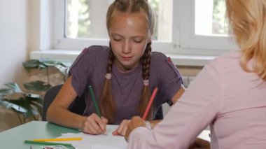 Saçları örülmüş kendini adamış bir öğrenci, özenli öğretmeninden cesaret alarak sanat projesine dalmış durumda. Bu canlı sınıf sahnesi yaratıcılığın sevincini ve öğrenci ile akıl hocası arasındaki bağları vurguluyor.