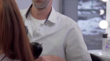 Modern bir güzellik salonunda yeni bir saç stili elde eden ışıl ışıl bir kadın. Saçları usta bir kuaför tarafından ustalıkla kurutulmuş. Bu canlı sahne, kendine bakmanın ve dönüşümün özünü yansıtıyor, sanatın sanatını gözler önüne seriyor.