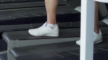 Kolsuz gömlekli kararlı bir adam koşu bandında rahatça yürür. Antrenmanını akıllı telefon ile dengede tutar. Bu dinamik sahne, modern fitness 'in özünü yakalıyor. Teknoloji, canlı bir spor salonunda adanmışlıkla buluşuyor.