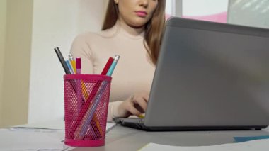 Kesilmiş bir atış, çalışmalarını yaparken parlak pembe bir bardak tutacağından kalem almaya çalışan kararlı bir üniversite öğrencisini yakalar. Notlar ve dizüstü bilgisayarla çevrili halde akademik başarı ve yaratıcılık ruhunu somutlaştırıyor.