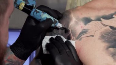 Karmaşık dövmelerle süslenmiş odaklanmış bir dövme sanatçısı müşterisinin omzuna ustalıkla mürekkep sürüp vücut sanatının sanatını sergiliyor. Canlı stüdyo atmosferi, detaylara titiz bir şekilde bakılması ve yaratıcılığın...