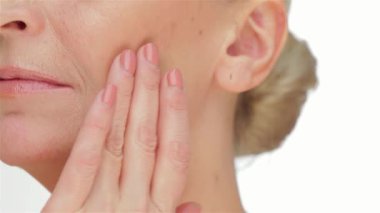 Zarif, yaşlı bir kadın pırıl pırıl yüzünü okşar. Kusursuz, taze cildini el değmemiş beyaz bir arka plana gösterir. Bu samimi an, onun doğal güzelliğini ve cilt bakımının özünü vurguluyor. İzleyicileri özgüvene davet ediyor.