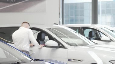 Şık bir işadamı, parlak araçlarla çevrili çağdaş bir bayilikte çarpıcı mavi bir otomobili inceliyor. Bu dinamik sahne araba alışverişinin heyecanını yakalıyor. Lüks ve satın almanın cazibesini gösteriyor.