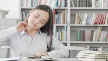 Güzel bir Asyalı kadın, serin bir kütüphanede kitap yığınlarıyla çevrili sırtını germek için biraz zaman harcar. Bu sahne, yaklaşan sınavlarına kararlılıkla hazırlanırken kendini adamanın ve bilgi arayışının özünü yakalıyor.