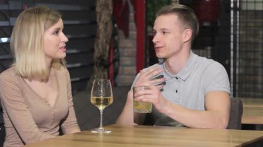 Hoş genç bir çift şık bir restoranda, sarışın adamın viskinin tadını çıkarırken sarışın kadının bir bardak beyaz şarabın tadını çıkardığı samimi bir anı paylaşıyor. Neşeli ifadeleri ve çekici konuşmaları sıcak bir atmosfer yaratıyor.