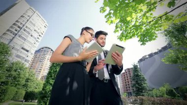 Kendine güvenen bir işadamı ve başarılı bir iş kadını, modern mimariyle çevrili kentsel bir ortamda tabletleri kullanırken canlı bir tartışmaya girişirler. Gülüşleri işbirliğinin ve başarının sevincini yansıtıyor.