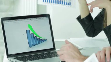 Kendine güvenen bir iş adamı ve profesyonel bir kadın şık bir laptopta satış verilerini incelerken canlı bir tartışmaya girişirler. Ekranda gösterilen yükseliş eğilimi büyüme ve başarıyı simgeleyerek bir işbirliği ve hırs ortamı yaratıyor.