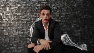 Keskin siyah bir takım elbise giymiş çarpıcı bir erkek vampir, kumlu tuğla bir duvara karşı lüks siyah bir kanepede oturuyor. Perili bakışları ve kan lekeli yüzü, ürkütücü bir Cadılar Bayramı atmosferini çağrıştırıyor. Gotik zerafetin özünü yakalamak için mükemmel.