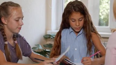 İki hevesli genç kız, renkli çizimlerini özenli bir öğretmene göstermek için sanat derslerine dalmış durumdalar. Bu canlı sahne yaratıcılığın ve işbirliğinin özünü yansıtıyor, kızlar hayal güçlerini ve