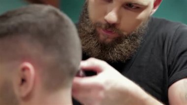 Şık bir berber dükkanında, yetenekli bir berber titizlikle sakallı bir adamın saçını şekillendirir, tımar sanatını sergiler. Retro dekor ve sıcak ışıklandırmayla vurgulanan samimi atmosfer, kişisel bakım ve dönüşüm deneyimini geliştirir.