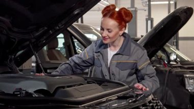 Becerikli ve çekici bir kadın araba tamircisi iyi aydınlatılmış bir garajda modern bir cipin motorunu özenle inceliyor. Odaklanmış ifadesi ve şık kızıl saçı otomotiv endüstrisine olan güvenini ve uzmanlığını gözler önüne seriyor.