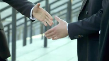 Bir grup güler yüzlü iş adamı şık resmi kıyafetler içinde sıcak bir tokalaşma içinde, hareketli bir şehir caddesinde başarılı bir ortaklığı sembolize ediyorlar. Atmosfer heyecan ve fırsatlarla dolu. Yeni başlangıçları kutluyorlar.