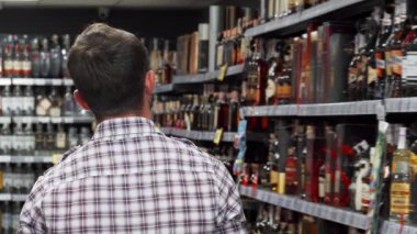 Dikiz ayarı, düzgün düzenlenmiş süpermarket raflarından şarap seçen bir adamı derinden yakalar. Mağazaların altında canlı şişeler ışıldıyor. Şarap meraklıları ve sıradan müşteriler için davetkar bir ortam yaratıyor.