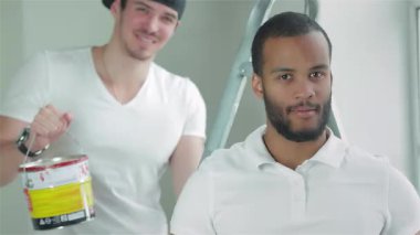 Parlak, boş bir dairede, genç bir işçi, arkadaşı bir sonraki görevi üstlenmeye hazır bir şekilde merdivenin üzerinde dururken, kendinden emin bir şekilde başparmağını kaldırır. Bu canlı sahne takım çalışmasının ve kararlılığın özünü yansıtıyor.