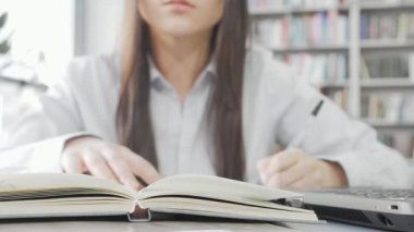 Kendini adamış bir kız öğrenci, rahat bir kütüphane ortamında edebiyatla dolu raflarla çevrili bir kitap okumaya derinden bağlıdır. Not defteri açık ve yanında bir dizüstü bilgisayarla akademik takip ve kararlılık ruhunu somutlaştırıyor.