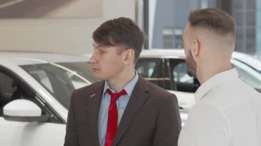 Tecrübeli bir erkek araba satıcısı müşterisine sıcak bir şekilde yaklaşır ve ona yeni bir araç seçme sürecinde rehberlik eder. Pürüzsüz otomobillerle dolu modern bayilik ortamı, önemli alımlar yapmak için davetkar bir ortam yaratıyor.