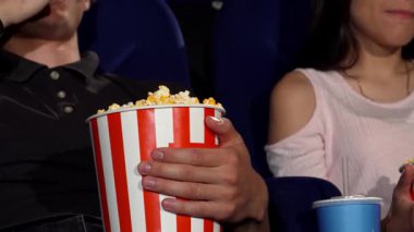 Sıcak bir çekim, sinemadaki bir film galasının heyecanına dalmış, büyük bir kova patlamış mısırı paylaşan bir adam ve kadını yakalar. Neşeli ifadeleri romantizmin sıcaklığını ve paylaşılan anların heyecanını yansıtıyor.