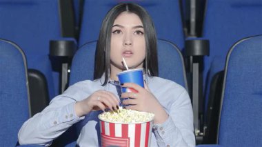 İç gözlemci bir Asyalı kadın canlı bir sinemada tek başına oturmuş patlamış mısırın ve gazozun tadını çıkarıyor. Parlak mavi koltuklar ve titreyen ekran, sinema için mükemmel bir atmosfer yaratıyor.
