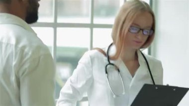 Parlak bir klinikte, şefkatli bir doktor sıcak ve profesyonel bir atmosfer sergileyen Afrikalı hastasını dikkatle dinler. Boynunda steteskopla özenle bir reçete yazıyor. Sağlık hizmetleri ve uzmanlığı somutlaştırıyor.