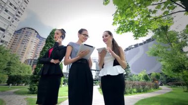 Canlı bir şehir parkında, üç kendine güvenen iş kadını işbirliğini geliştirmek için tablet ve telefonları kullanarak dinamik tartışmalara girişiyor. Şık kıyafetleri ve ışıl ışıl gülümsemeleri profesyonelliği ve başarıyı yansıtıyor.