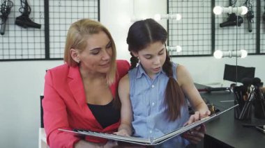 Canlı bir güzellik salonunda, sevimli küçük bir kız şık annesinin renkli bir paletten mükemmel saç rengini seçmesine hevesle yardımcı olur, neşe ve bağlantı yayar. Bu yürek ısıtan sahne anneliğin ve hoş bağın özünü yansıtıyor.