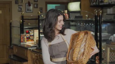 Neşeli bir dişi fırıncı kameraya ışıldıyor, güzel örülmüş bir sepet dolusu altın, kabuklu taze ekmek tutuyor. Bu canlı sahne sanatsal pişirmenin özünü yakalar, müşterileri sıcaklığa ve aromaya davet eder.