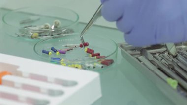 Yetenekli bir dişçi, eldivenli ve odaklanmış, titizlikle steril bir tepside dişçi aletleri ayarlar, gelecek tedaviye hazır. Bu görüntü, dişçi işlemlerinde gösterilen hassasiyet ve özeni yakalar ve gerekli aletleri gösterir.