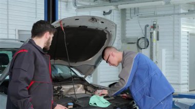 Hareketli bir araba servis istasyonunda, mavi üniformalı genç sarışın bir tamirci, siyah üniformalı esmer ortağı ona aletler verirken, özenle bir araç motoruna sorun çıkarıyor. Sahne, takım çalışmasının ve uzmanlığın özünü yakalıyor.
