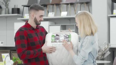 Tarz sahibi genç bir çift, modaya uygun ekose gömlekli bir adam ve sıradan kot ceketli bir kadın, modern bir mobilya mağazasında ortopedik bir yatak örnekleri inceliyor. Paylaştıkları gülücükler ve nişanlı ifadeleri,