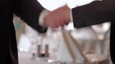 Şık bir restoran ortamında, iki iyi giyimli iş adamı el sıkışıyor ve başarılı bir ortaklık kuruyorlar. Yumuşak ışıklandırma ve düzgünce düzenlenmiş tablolarla birlikte zarif ortam, işbirliği ve karşılıklı işbirliği atmosferini geliştirir.