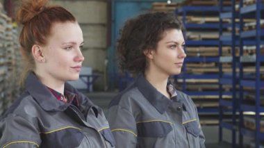 Koruyucu şapkalarla süslenmiş iki yetenekli genç bayan mühendis, yoğun bir metal deposuna güvenle ışınlanıyorlar. Canlı gülümsemeleri ve profesyonel kıyafetleri sanayi sektöründeki güç ve takım çalışmasını yansıtıyor.