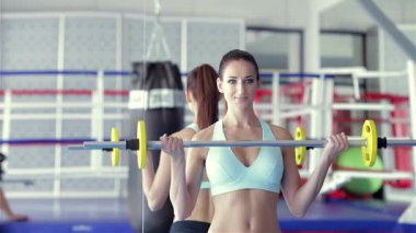 Şık, açık mavi bir spor sutyen giymiş kararlı genç bir kadın canlı bir spor salonunda halteri kaldırır ve eğitime hazırdır. Spor hocası, ringde yapılacak yoğun bir boks seansına hazırlanırken onu cesaretlendiriyor.