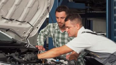 Becerikli bir tamirci yakışıklı bir erkek müşteriyle dostça sohbet ederek otomobil motorunu özenle tamir eder. Sahne profesyonellik ve güvenin özünü yakalıyor, mekanik uzmanlığını iyi donanımlı bir şekilde gösteriyor.