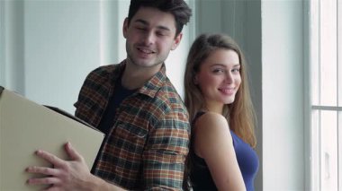 Neşeli bir çift kutuları taşırken karton bir kutuyu tutarken birbirlerine sevgiyle bakıyorlar. Gülüşleri mutluluk saçıyor, rahat dairelerinde yeni bir sayfa açmanın heyecanını simgeliyor.