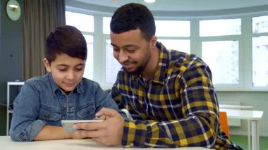 Siyah saçlı neşeli genç bir çocuk, babasının akıllı telefonundaki resimlere hevesle göz atar. İkisi de teknolojinin büyüleyici dünyasına dalmıştır. Yakışıklı Afrikalı Amerikalı baba oğluyla tatlı bir anı paylaşıyor. Aralarındaki bağı gösteriyor.