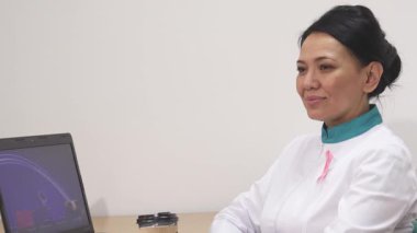 Tuğla aksanlı, gevrek beyaz bir ceket giymiş, dingin, olgun bir kadın doktor, ofisinde dinleniyor, düşünceli bir şekilde uzaktan bakarken sıcak bir fincan kahvenin tadını çıkarıyor. Bu sakin sahne, özbakımın ve yansımanın özünü yakalar.