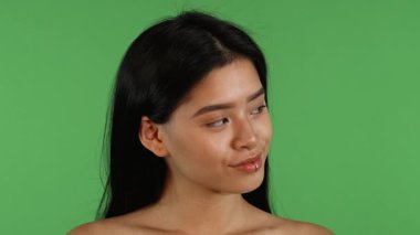Büyüleyici genç bir Asyalı kadın, kameraya parlak bir şekilde gülümsemeden önce uzun koyu renk saçlarını zarifçe dalgalandırarak kenarlara bakar. Bu büyüleyici an, canlı yeşil bir kromatuara karşı dizilmiş güven ve kadınlığı yayar.