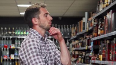 Düşünceli bir ifadeye sahip yakışıklı bir adam iyi stoklanmış bir süpermarket koridorunda canlı bir dizi şarap şişesini inceliyor. Anlayışlı bakışları, seçimlerini dikkatli bir şekilde düşünürken, modern bir ruhun özünü somutlaştıran kalite tutkusunu yansıtıyor.