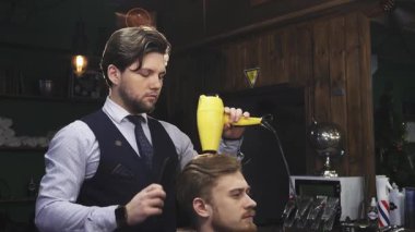 Şık, sakallı bir berber, müşterilerinin saçlarını rahat bir berber dükkanında şekillendirmek için parlak sarı saç kurutma makinesini ustalıkla kullanır. Sıcak atmosfer ve klasik dekor, berberlik ve berberlik arasındaki bağın sanatsal özelliklerini gösteren hoş bir atmosfer yaratıyor.